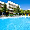 Piscina circondata da lettini blu e ombrelloni, edificio bianco a più piani sullo sfondo.